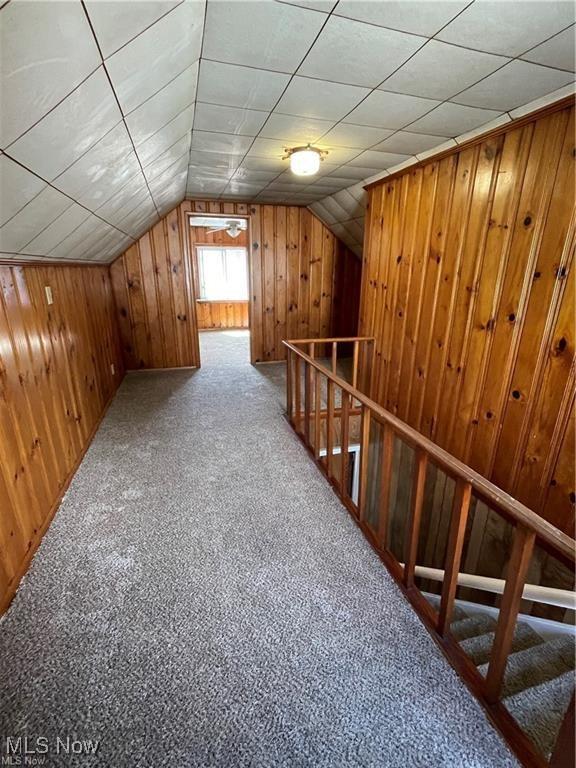 bonus room with wooden walls, carpet, and lofted ceiling