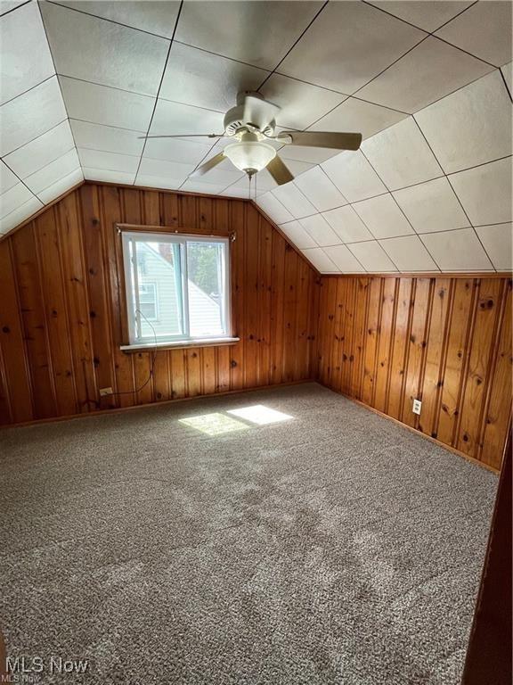 additional living space featuring carpet flooring, vaulted ceiling, ceiling fan, and wood walls