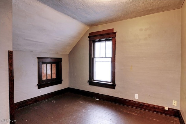 additional living space with dark hardwood / wood-style flooring, lofted ceiling, and a textured ceiling