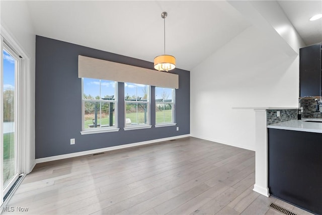 unfurnished dining area featuring light wood-type flooring, vaulted ceiling, and sink