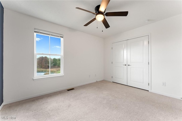 unfurnished bedroom with light carpet, a closet, and ceiling fan