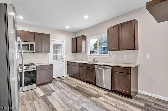 kitchen featuring dark brown cabinetry, sink, light wood-type flooring, and appliances with stainless steel finishes