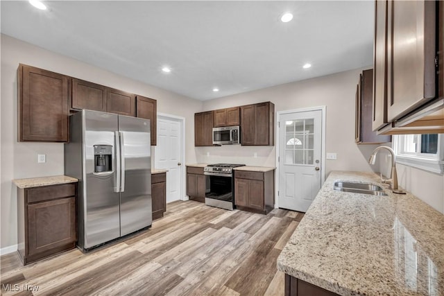 kitchen featuring sink, light stone countertops, light hardwood / wood-style floors, dark brown cabinetry, and stainless steel appliances