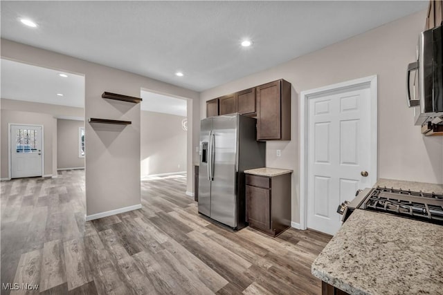 kitchen featuring dark brown cabinets, light hardwood / wood-style floors, light stone counters, and stainless steel appliances