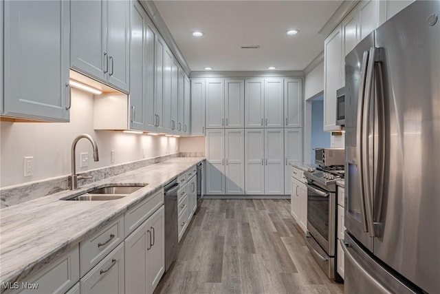 kitchen with white cabinetry, light stone countertops, sink, light hardwood / wood-style flooring, and appliances with stainless steel finishes