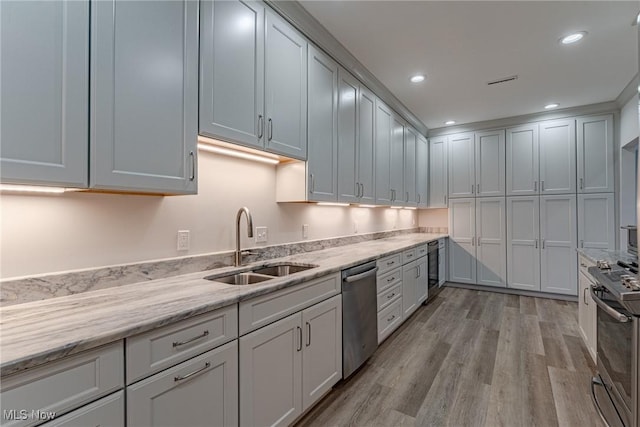 kitchen with appliances with stainless steel finishes, light stone counters, light hardwood / wood-style flooring, and sink