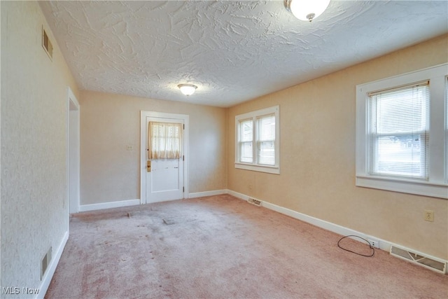 unfurnished room featuring a textured ceiling, light colored carpet, and a healthy amount of sunlight