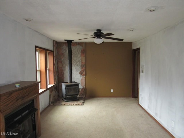 unfurnished living room featuring light carpet, a wood stove, and ceiling fan