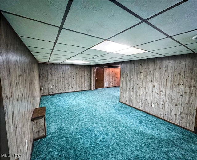 basement featuring carpet flooring, a paneled ceiling, and wood walls