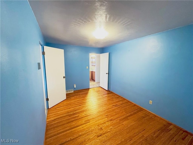 empty room with light wood-type flooring and a baseboard heating unit