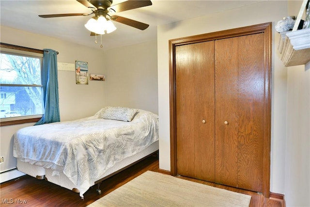 bedroom with dark hardwood / wood-style flooring, ceiling fan, a closet, and a baseboard heating unit