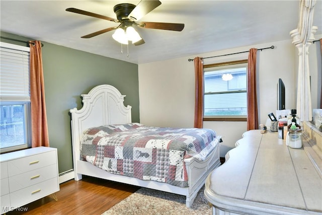 bedroom with dark hardwood / wood-style flooring, baseboard heating, and ceiling fan