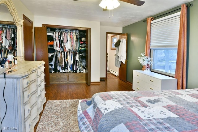 bedroom featuring ceiling fan, baseboard heating, dark hardwood / wood-style floors, multiple windows, and a closet