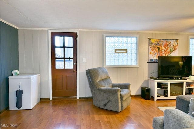 living room featuring crown molding, plenty of natural light, wood-type flooring, and wood walls