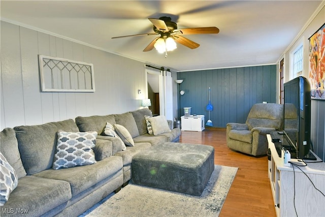 living room with a barn door, wood-type flooring, crown molding, and wooden walls