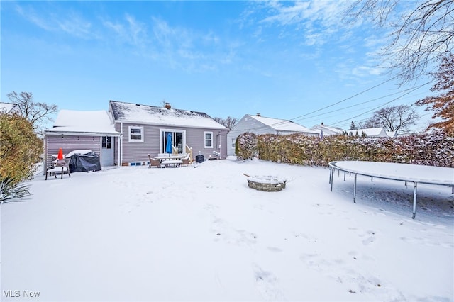 snow covered back of property with a trampoline and an outdoor structure