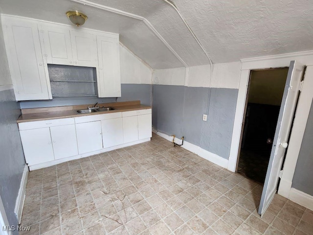 kitchen with a textured ceiling, white cabinetry, sink, and vaulted ceiling