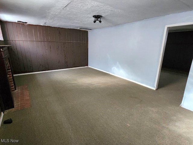 basement with carpet flooring, wooden walls, a textured ceiling, and a brick fireplace