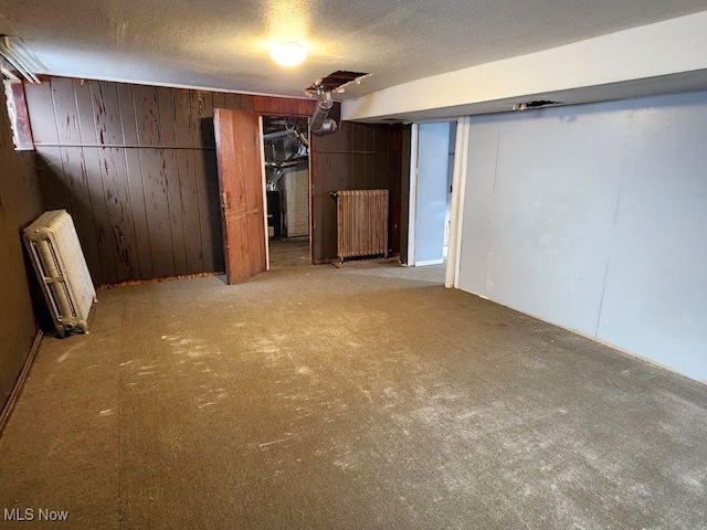 basement with wood walls, light colored carpet, radiator heating unit, and a textured ceiling