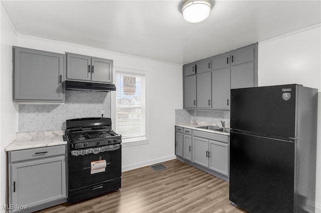 kitchen with sink, tasteful backsplash, light hardwood / wood-style floors, gray cabinets, and black appliances