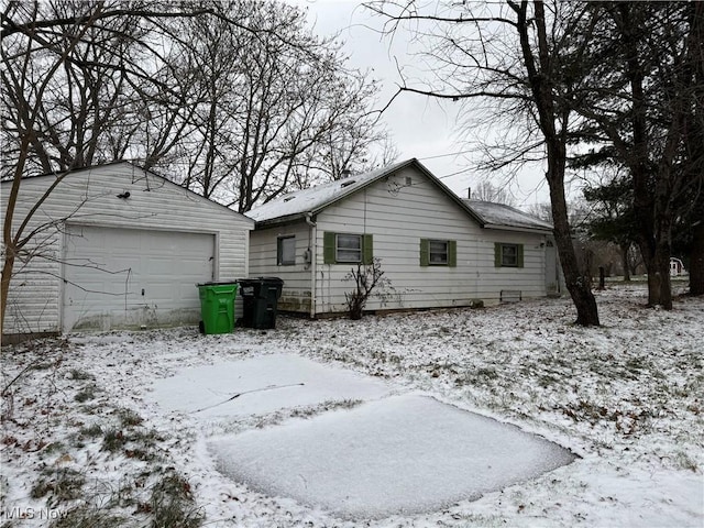 snow covered rear of property featuring a garage and an outbuilding