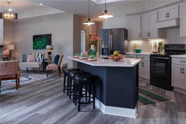 kitchen featuring black electric range, dark hardwood / wood-style floors, a kitchen island with sink, and refrigerator with ice dispenser