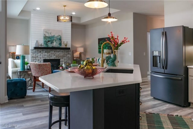 kitchen featuring light hardwood / wood-style flooring, pendant lighting, stainless steel refrigerator with ice dispenser, and a center island with sink