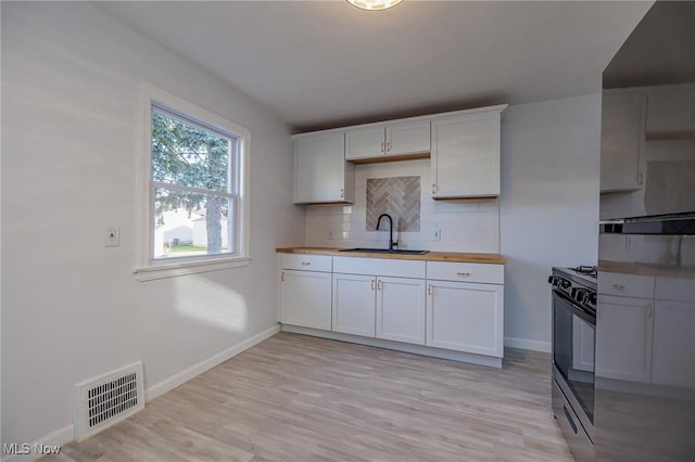 kitchen with butcher block counters, white cabinetry, sink, and black stove