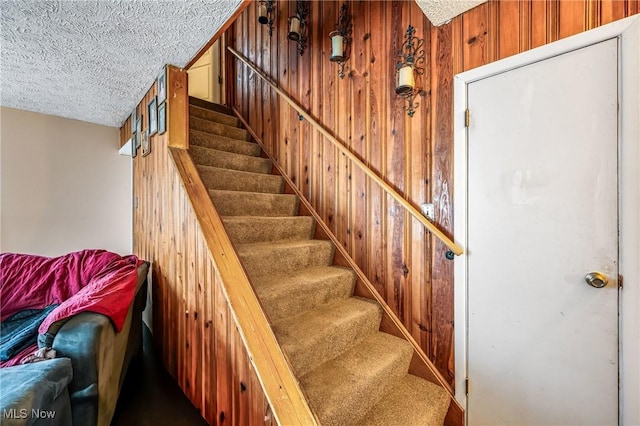 staircase with wood walls and a textured ceiling