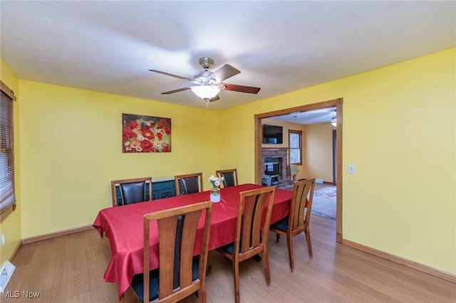 dining area with ceiling fan, light wood-type flooring, and a brick fireplace