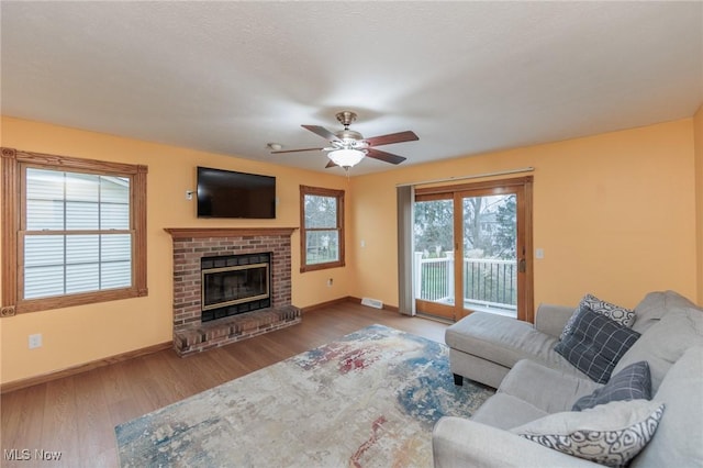 living room with hardwood / wood-style floors, ceiling fan, a wealth of natural light, and a brick fireplace