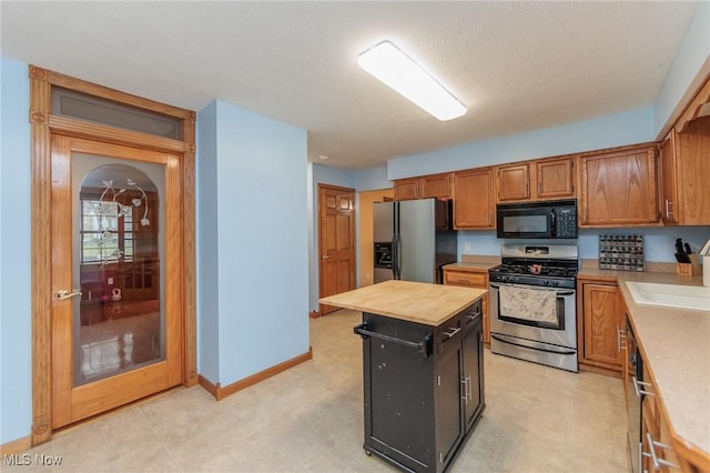 kitchen with appliances with stainless steel finishes, a textured ceiling, sink, a center island, and butcher block countertops