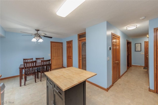 kitchen with ceiling fan, a kitchen island, light tile patterned flooring, and a textured ceiling