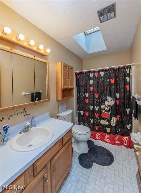 bathroom featuring vanity, a skylight, toilet, a textured ceiling, and curtained shower