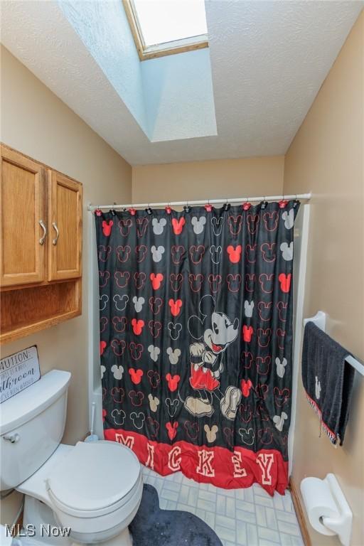 bathroom with a skylight, a shower with curtain, a textured ceiling, and toilet