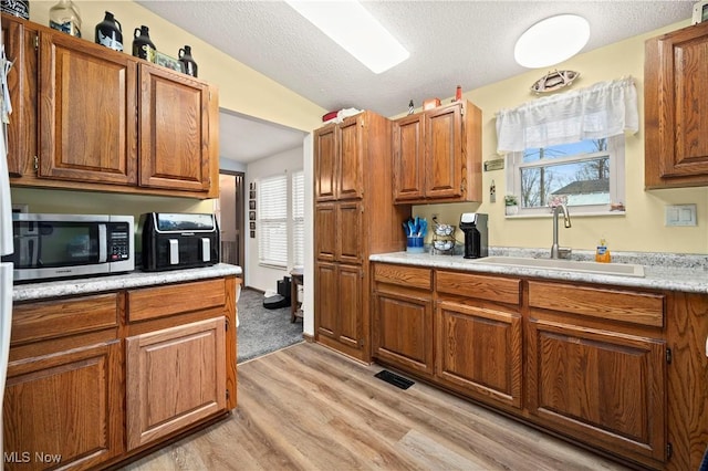 kitchen featuring a textured ceiling, light hardwood / wood-style floors, lofted ceiling, and sink