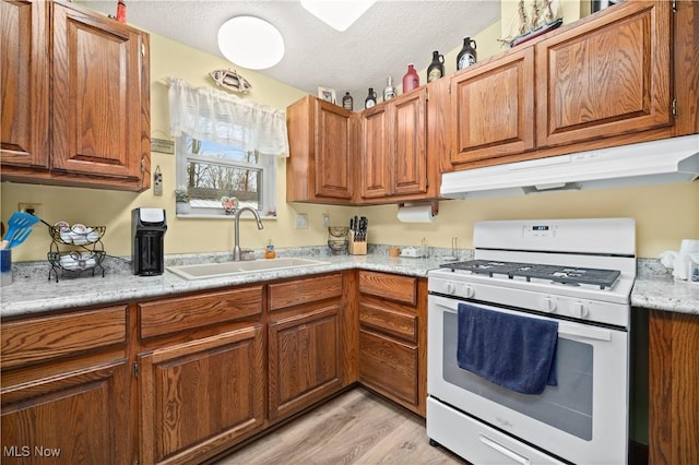 kitchen with sink, white range with gas stovetop, a textured ceiling, and light hardwood / wood-style floors