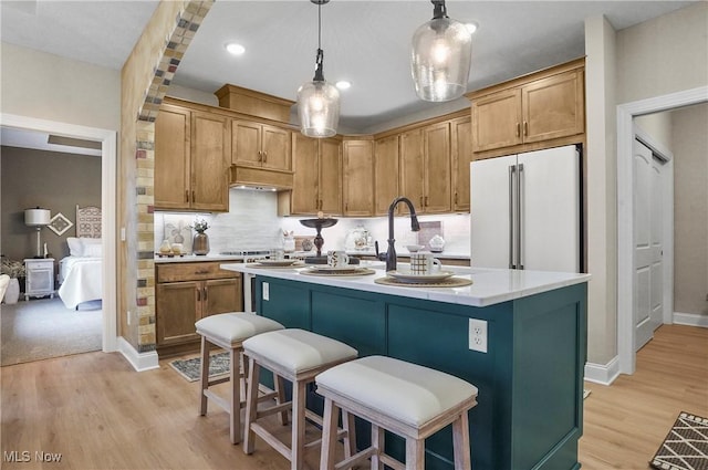 kitchen with pendant lighting, backsplash, high end white fridge, an island with sink, and light hardwood / wood-style floors