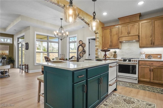 kitchen with a chandelier, decorative light fixtures, a kitchen island with sink, stainless steel stove, and light wood-type flooring