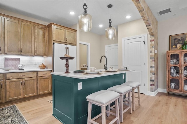 kitchen featuring hanging light fixtures, high end white fridge, a kitchen island with sink, a breakfast bar, and light wood-type flooring