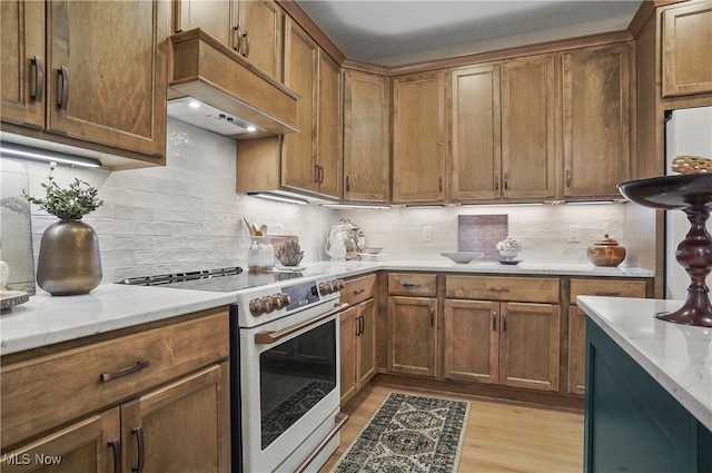 kitchen with backsplash, premium range hood, light stone counters, high end white range oven, and light hardwood / wood-style flooring