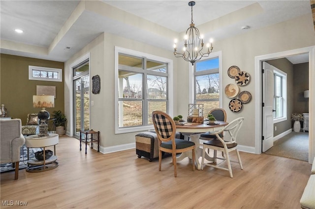 dining area featuring a notable chandelier, a raised ceiling, and light hardwood / wood-style flooring