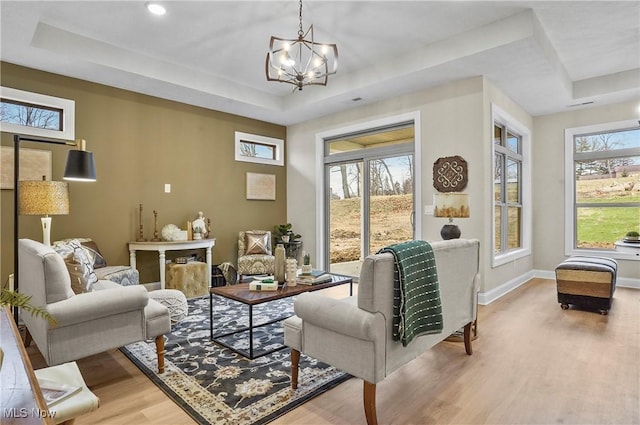 sitting room featuring a chandelier, a healthy amount of sunlight, wood-type flooring, and a tray ceiling