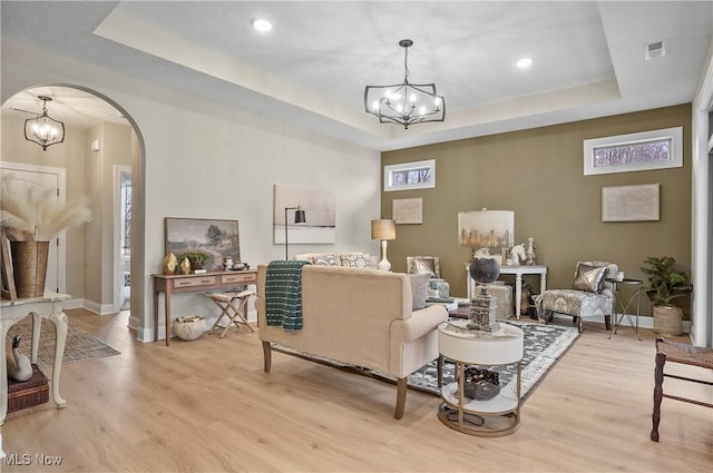 living room featuring a raised ceiling, a chandelier, and light wood-type flooring