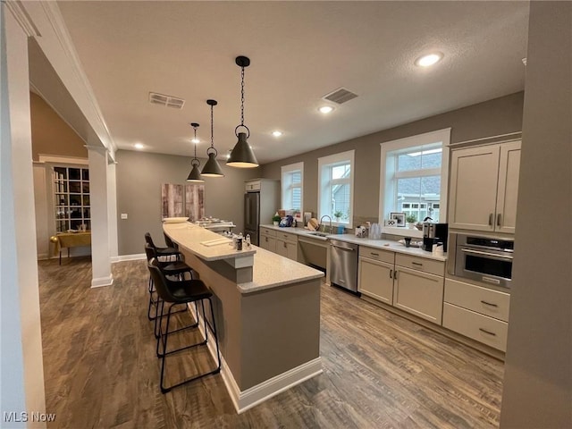 kitchen with a center island with sink, light stone countertops, appliances with stainless steel finishes, decorative light fixtures, and wood-type flooring