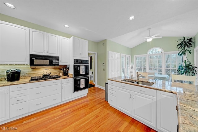 kitchen with sink, black appliances, light hardwood / wood-style floors, white cabinetry, and lofted ceiling