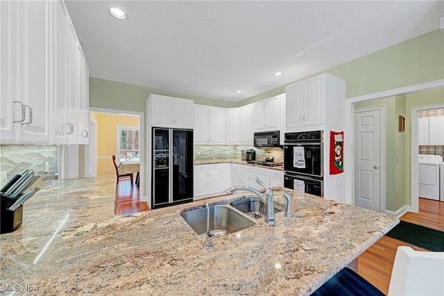 kitchen with black appliances, washer / dryer, kitchen peninsula, and sink