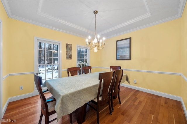 dining area featuring wood-type flooring, a tray ceiling, ornamental molding, and a notable chandelier