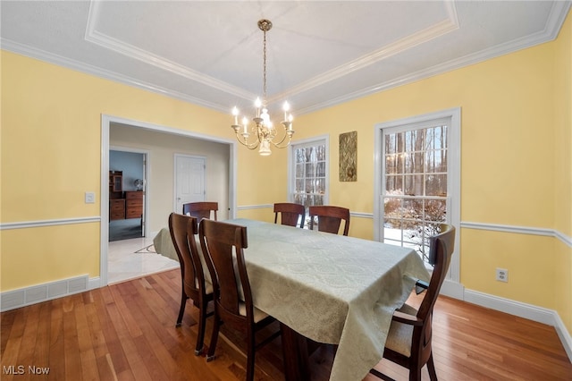 dining area with light wood-type flooring, a raised ceiling, and a healthy amount of sunlight