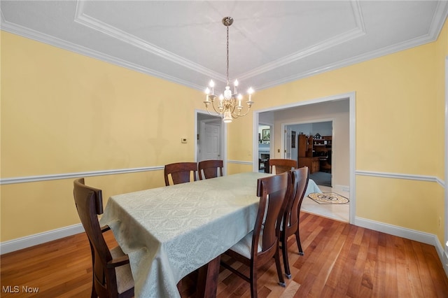 dining space featuring hardwood / wood-style floors, a raised ceiling, crown molding, and a chandelier